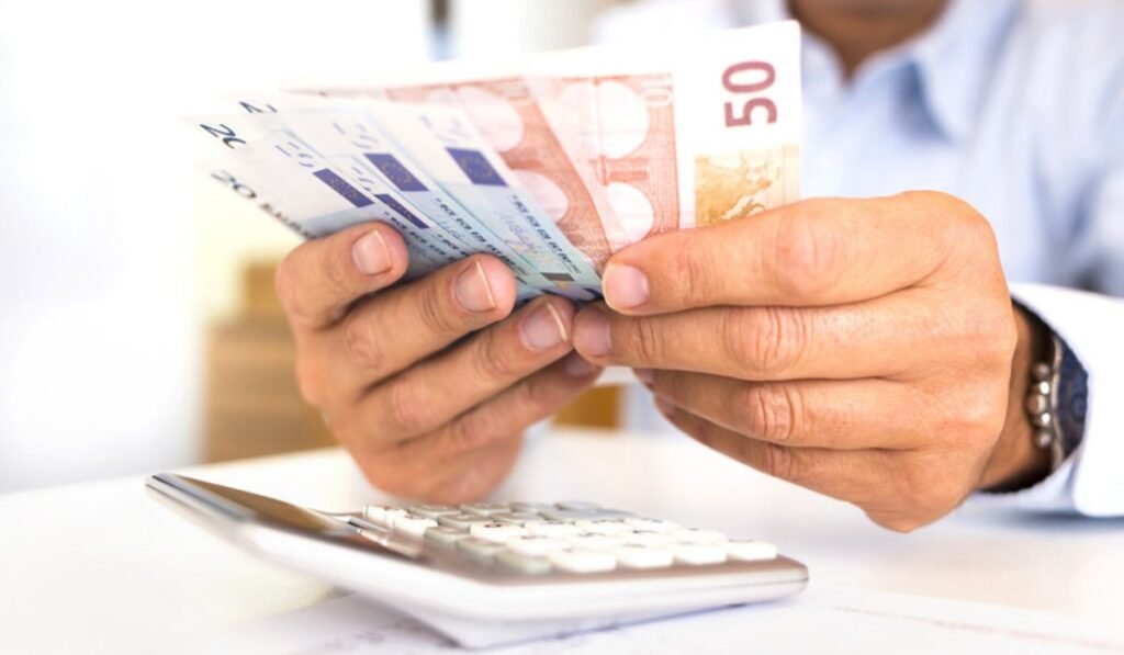 Άνδρας μετρά ευρώ δίπλα σε υπολογιστή